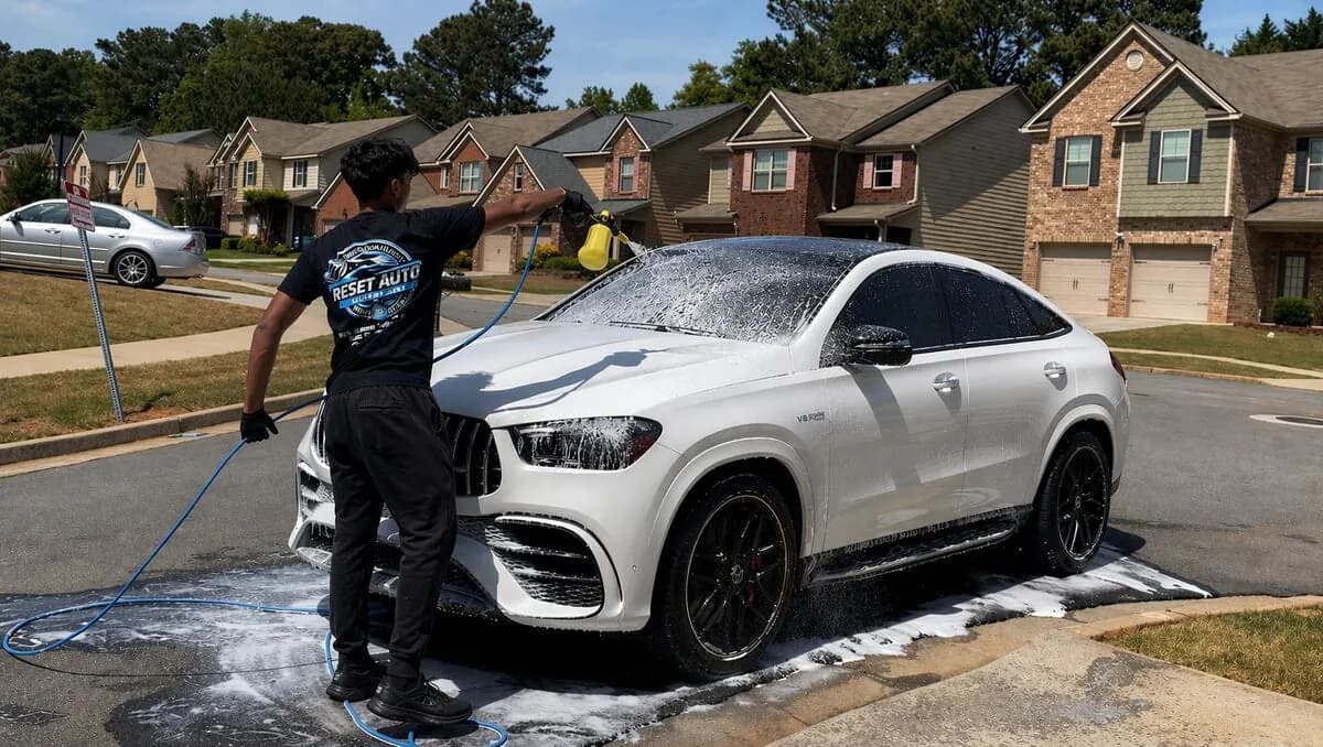 A Reset Auto Detailing technician foam-washing a white Mercedes SUV in a suburban driveway