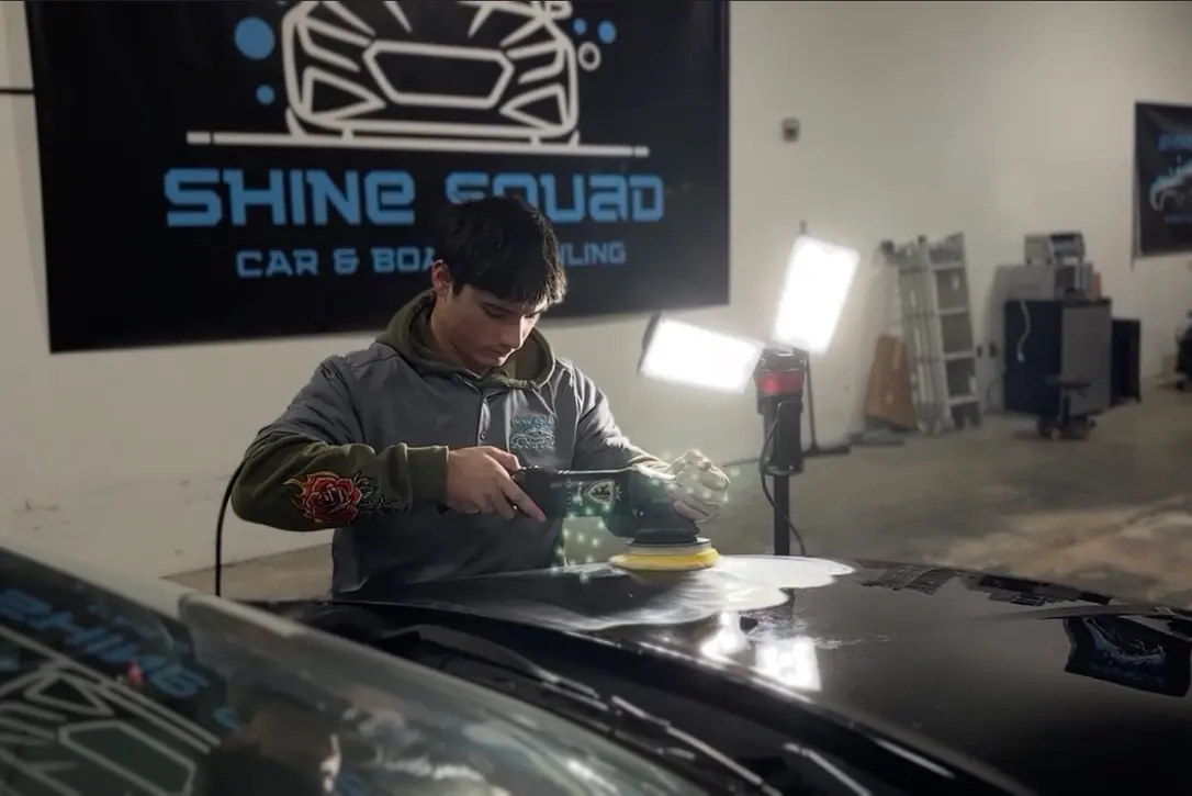 A Shine Squad technician machine-polishing the hood of a black car in the Shine Squad detailing shop