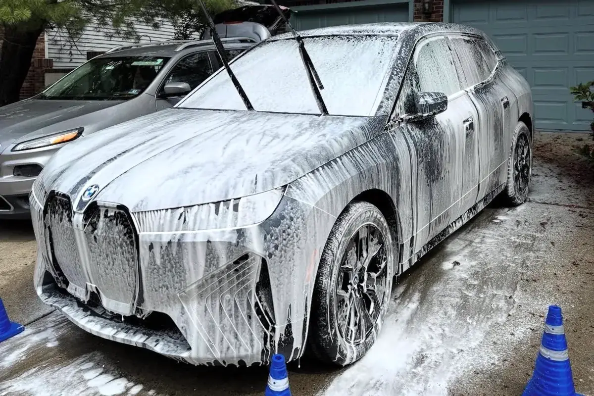 A foam-covered BMW SUV mid-wash in a residential driveway, with traffic cones marking the work area
